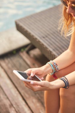 Bir yüzme havuzu güverte salonda yatarken cep telefonu kullanarak kız 
