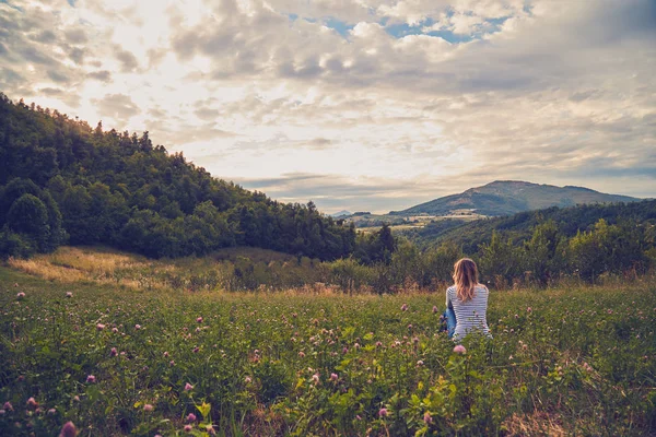 Ragazza seduta su un prato verde e guardando la terra di campagna — Foto Stock