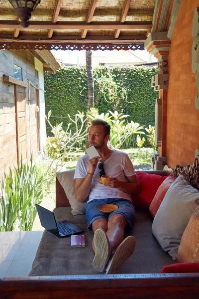 Hombre usando el teléfono celular y el ordenador portátil mientras bebe café / té en th — Foto de Stock