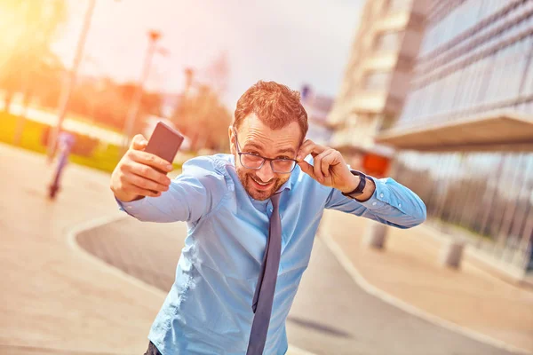 Divertido hombre de negocios con pulgares hacia arriba mientras usa el teléfono inteligente al aire libre —  Fotos de Stock