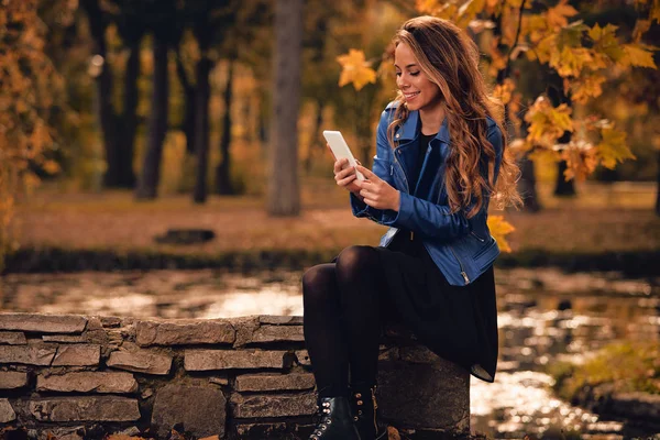 Menina bonito usando celular no parque com cores de outono . — Fotografia de Stock