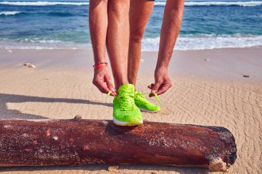 Bir tropikal egzotik plajda çalışan Sneakers bağlama adam.