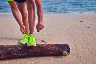 Bir tropikal egzotik plajda çalışan Sneakers bağlama adam.