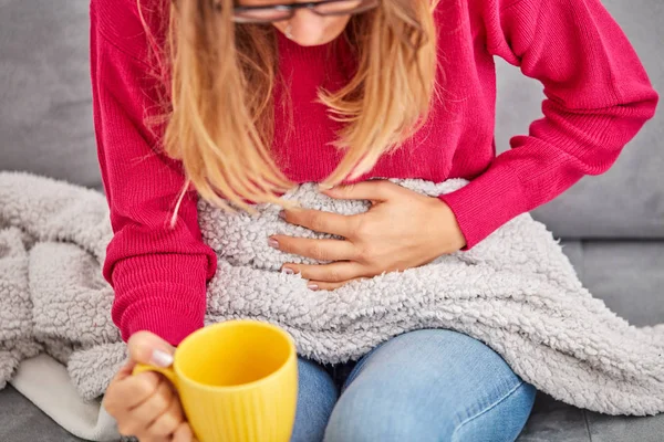 Niña enferma sosteniendo la taza y bebiendo café / té en un sofá . — Foto de Stock