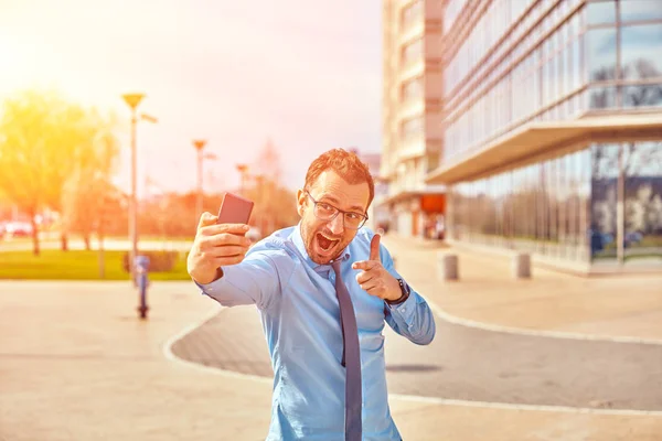 Divertido hombre de negocios con pulgares hacia arriba mientras usa el teléfono inteligente al aire libre —  Fotos de Stock