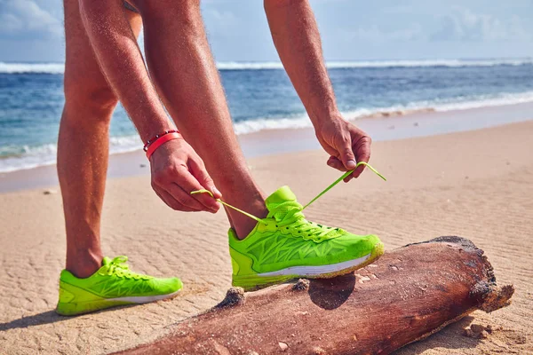 Bir tropikal egzotik plajda çalışan Sneakers bağlama adam.