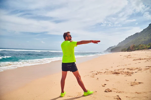 Deportista estirándose en una exótica playa tropical después de correr / —  Fotos de Stock