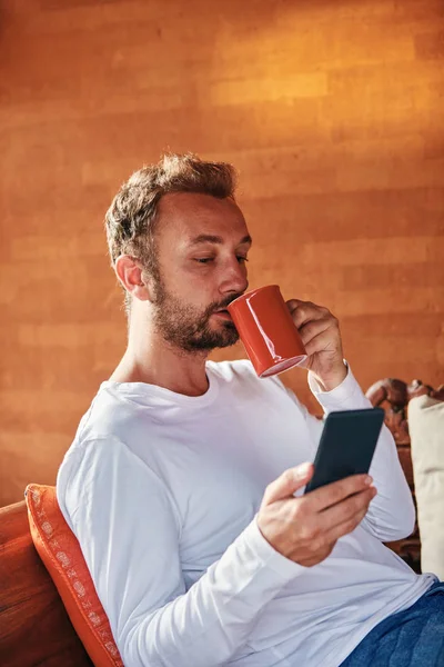 Hombre sentado en un sofá terraza y beber café / té mientras usa — Foto de Stock