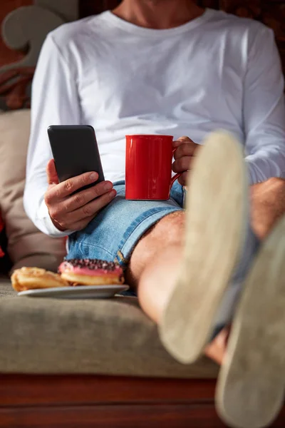 Hombre sentado en un sofá terraza y beber café / té, comer hacer — Foto de Stock