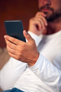 Teras kanepede oturan ve cep telefonu kullanan adam.