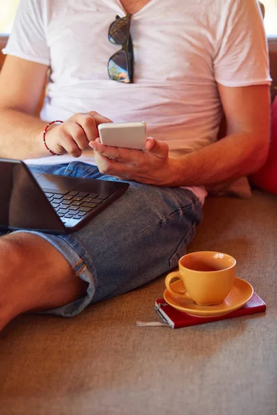 Hombre usando el teléfono celular y el ordenador portátil mientras bebe café / té en th — Foto de Stock