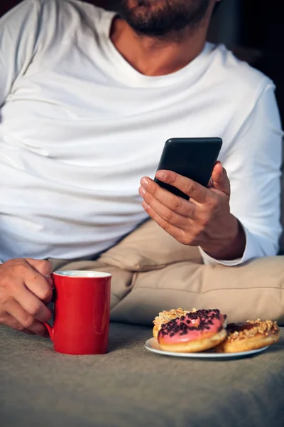 Hombre sentado en una terraza sofadrinking café y comer donuts w — Foto de Stock