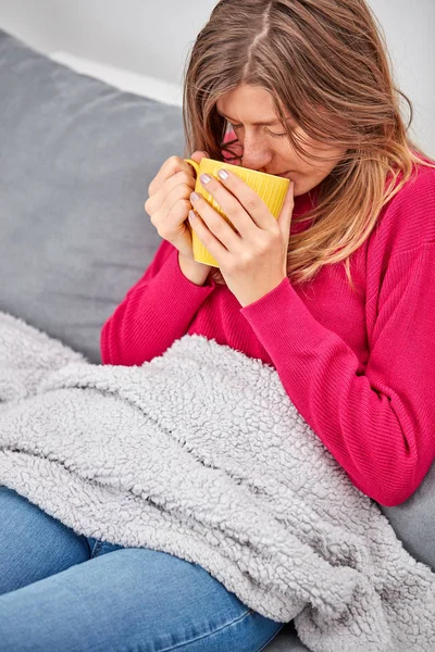 Nemocný děvče držící pohár a popíjení kávy/čaje na gauči. — Stock fotografie