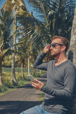 Cep telefonu kullanan adam / smartphone tropikal ortamda.