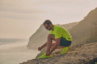 Tropik egzotik bir uçurumda koşu spor ayakkabısı bağlayan adam.