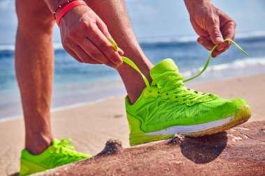 Bir tropikal egzotik plajda çalışan Sneakers bağlama adam.