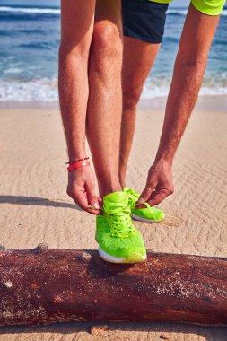 Bir tropikal egzotik plajda çalışan Sneakers bağlama adam.