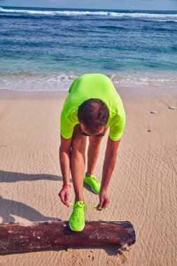 Bir tropikal egzotik plajda çalışan Sneakers bağlama adam.