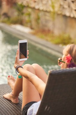 Bir yüzme havuzu güverte salonda yatarken cep telefonu kullanarak kız 