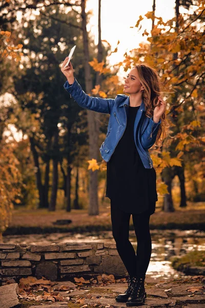 Aranyos lány segítségével cellphone-parkban őszi színek. — Stock Fotó