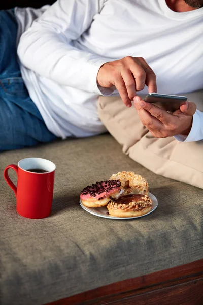 Hombre sentado en una terraza sofadrinking café y comer donuts w — Foto de Stock
