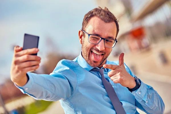 Divertido hombre de negocios con pulgares hacia arriba mientras usa el teléfono inteligente al aire libre —  Fotos de Stock