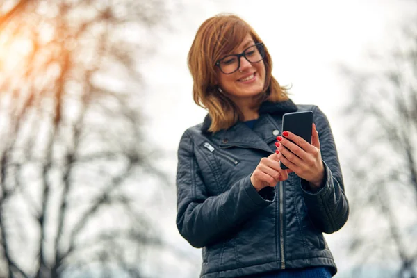 Linda mujer joven usando el teléfono celular al aire libre . — Foto de Stock