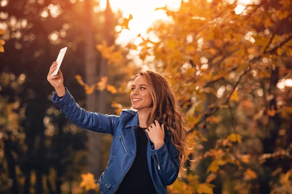 Aranyos lány segítségével cellphone-parkban őszi színek. — Stock Fotó