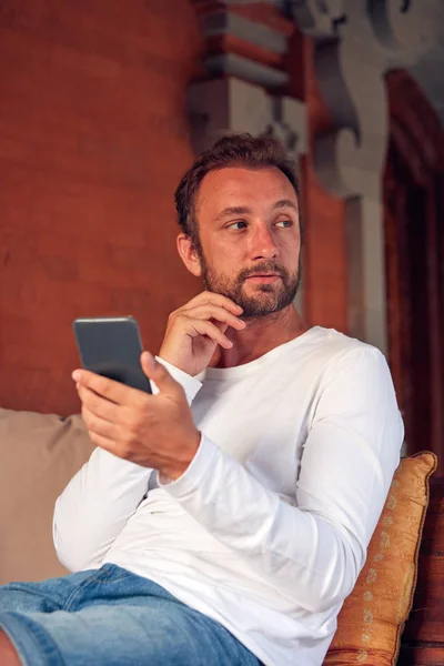 Hombre sentado en un sofá de la terraza y usando el teléfono celular . — Foto de Stock