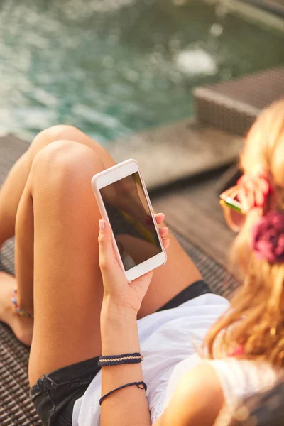 Chica usando el teléfono celular mientras está acostado en un salón de cubierta de piscina — Foto de Stock