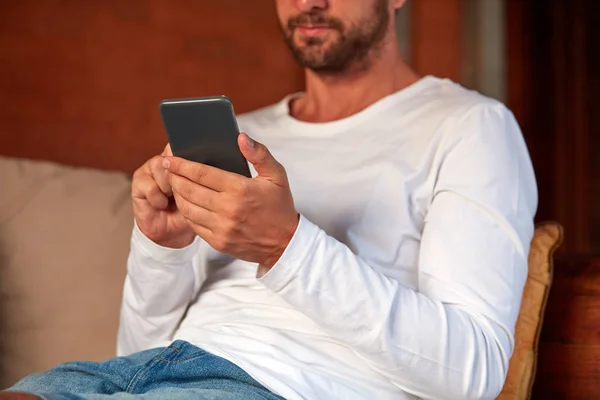 Hombre sentado en un sofá de la terraza y usando el teléfono celular . — Foto de Stock