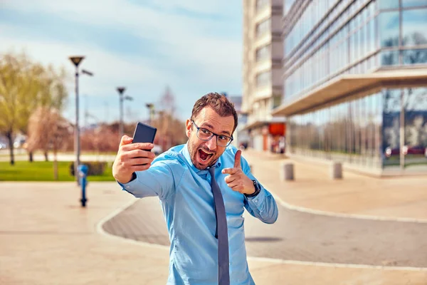 Divertido hombre de negocios con pulgares hacia arriba mientras usa el teléfono inteligente al aire libre —  Fotos de Stock