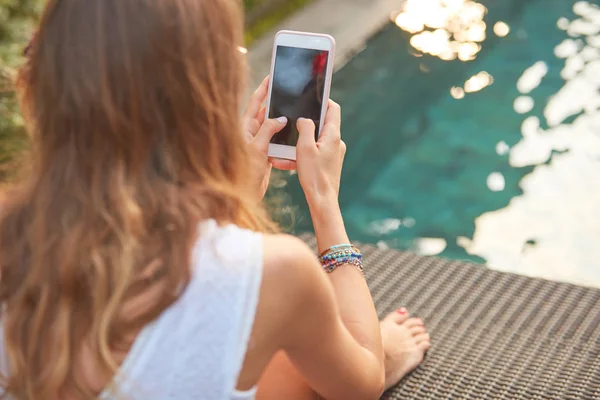 Дівчина використовує мобільний телефон, лежачи на вітальні басейну — стокове фото