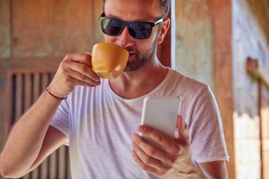 Verandada kahve/çay içerken cep telefonu kullanan adam.