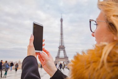 Paris geçmişi ve Eyfel kulesi olan cep telefonu kullanan bir kız.