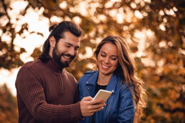 Genç çift sonbahar renkli park'cep telefonu kullanma.