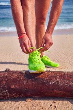 Bir tropikal egzotik plajda çalışan Sneakers bağlama adam.