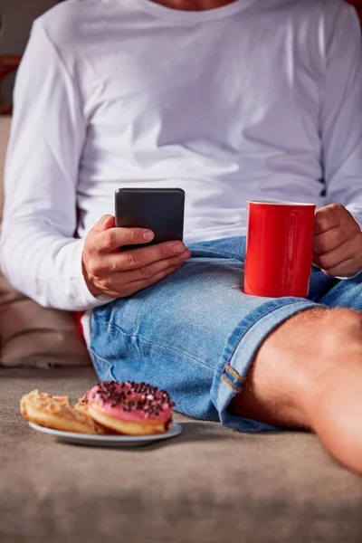 Hombre sentado en un sofá terraza y beber café / té, comer hacer — Foto de Stock