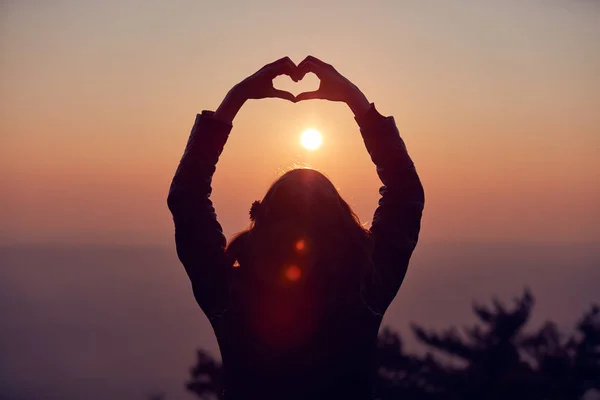 Girl making heart - shape sign with hands at sunset / sunrise ti