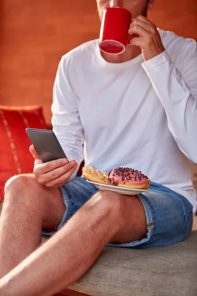 Hombre sentado en un sofá terraza y beber café / té, comer hacer — Foto de Stock