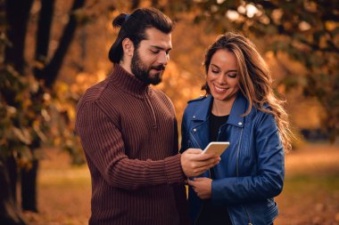 Genç çift sonbahar renkli park'cep telefonu kullanma.