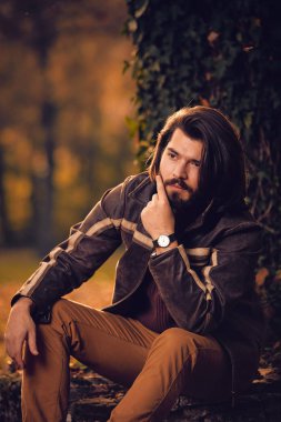 Sonbahar renkli parkta ağacın yanında oturan adam.