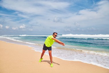 Sportsman stretching on a exotic tropical beach after jogging / 