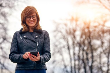 Sevimli genç kadın kullanarak Cellphone açık havada.