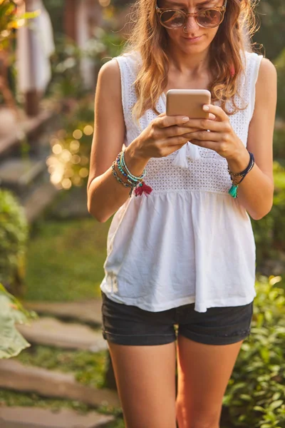 Vrouw met behulp van mobiele telefoon buitenshuis in het park/tuin. — Stockfoto