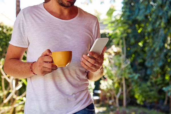 Homem usando celular enquanto bebe café / chá no alpendre . — Fotografia de Stock