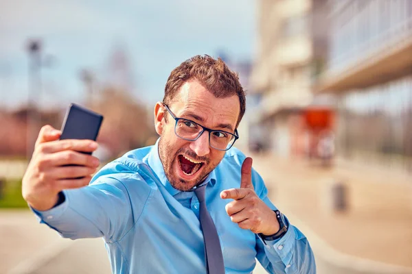 Divertido hombre de negocios con pulgares hacia arriba mientras usa el teléfono inteligente al aire libre —  Fotos de Stock