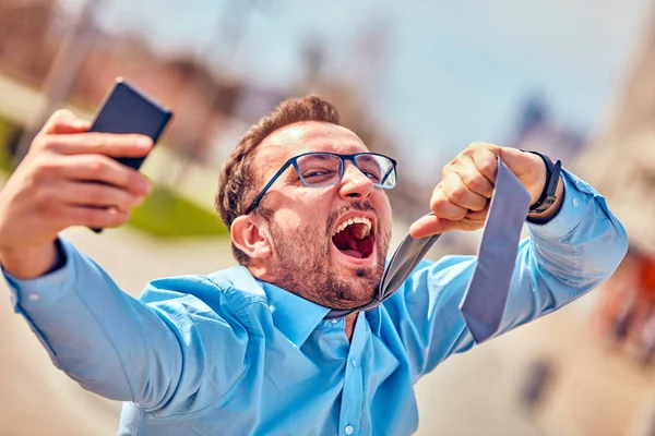 Divertido hombre de negocios enojarse mientras usa el teléfono inteligente al aire libre . —  Fotos de Stock