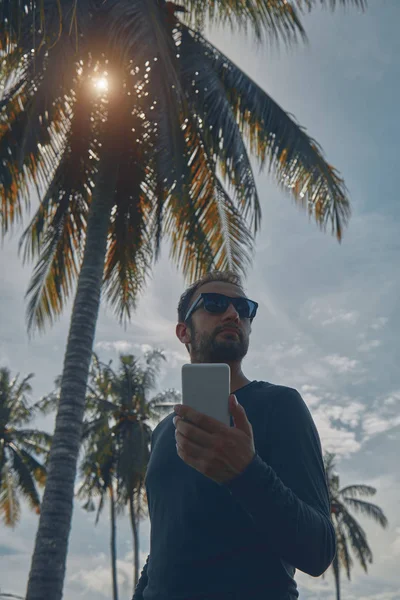 Hombre usando teléfono celular / smartphone en ambiente tropical . —  Fotos de Stock