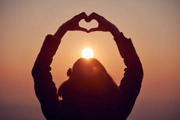 Dziewczyna robi serce kształt znak z rąk o zachodzie słońca/wschód TI — Zdjęcie stockowe